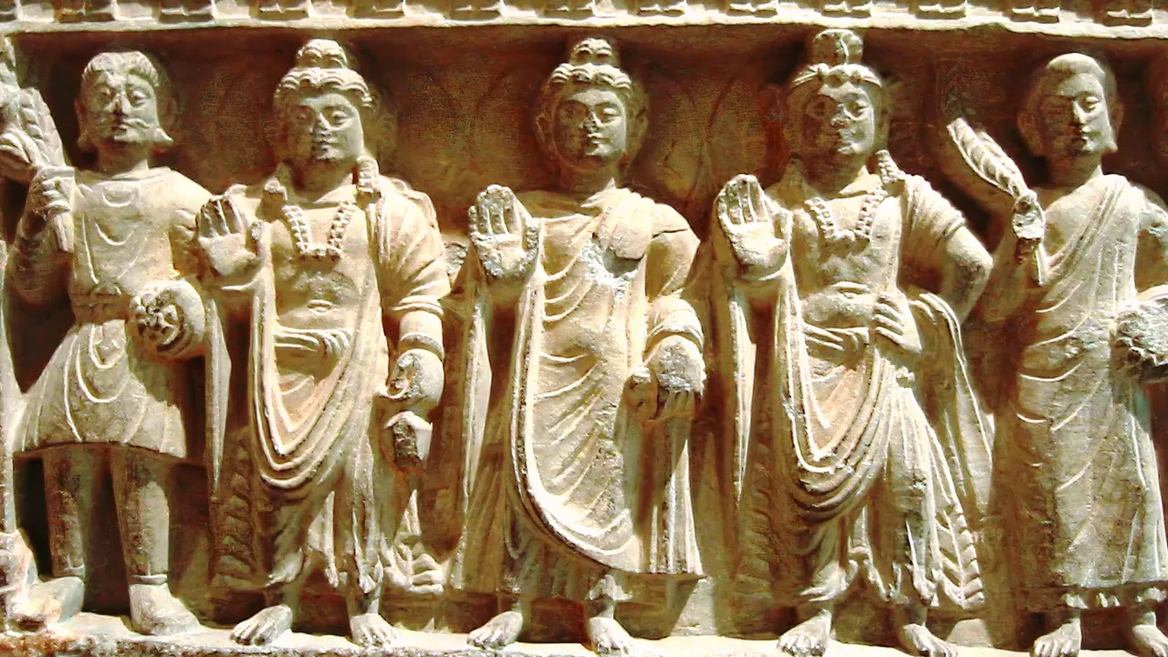 A carved relief panel depicting five figures in ancient attire, possibly from Gandhara art, showcasing detailed clothing and jewelry.