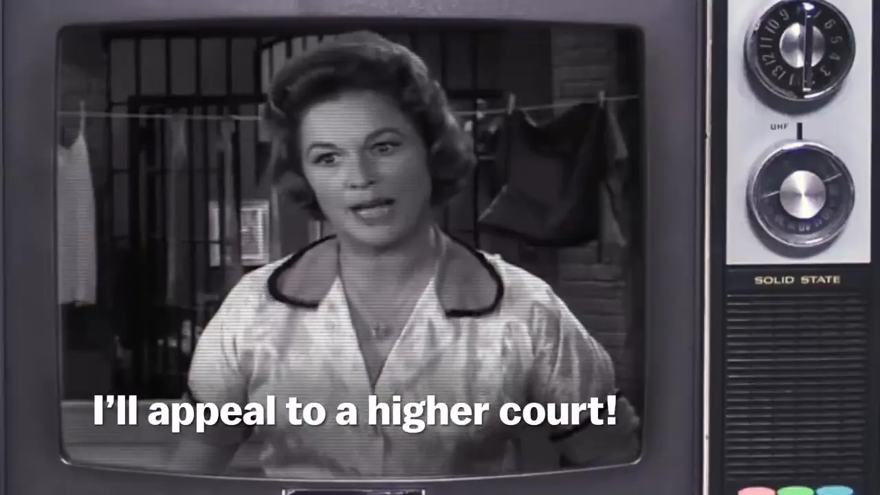 A black and white television screen shows a woman speaking with the text "I'll appeal to a higher court!" at the bottom.